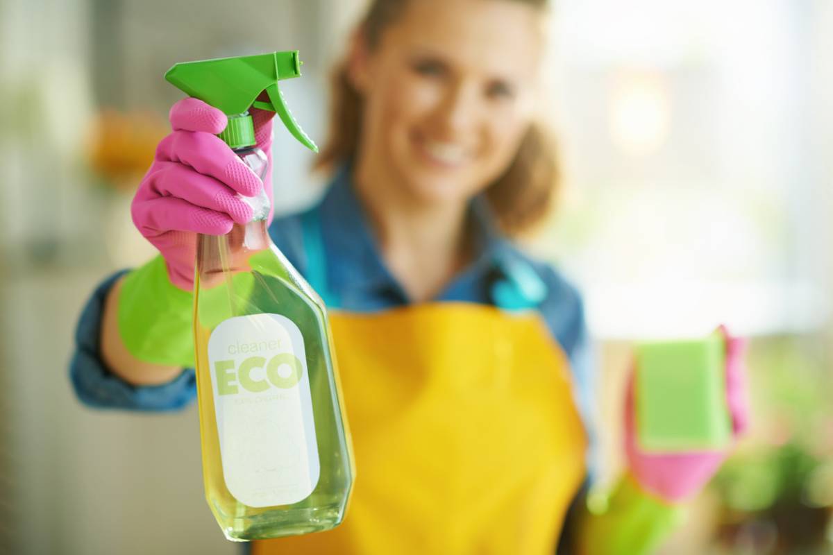 Agente d’entretien en gants roses tendant un spray nettoyant écologique Agente d’entretien en gants roses tendant un spray nettoyant écologique